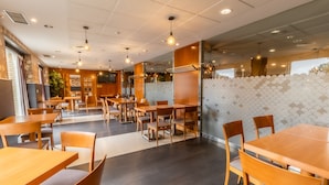Interior de restaurante con mesas y sillas de madera, un muro con diseño y un ventanal grande.