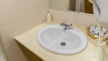 A bathroom with a white sink, a mirror, and a hairdryer on the counter.