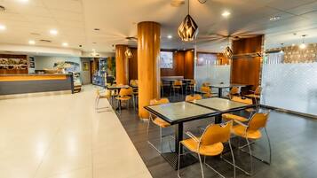 A spacious indoor area with multiple tables and chairs, a reception desk, and a counter with various items.