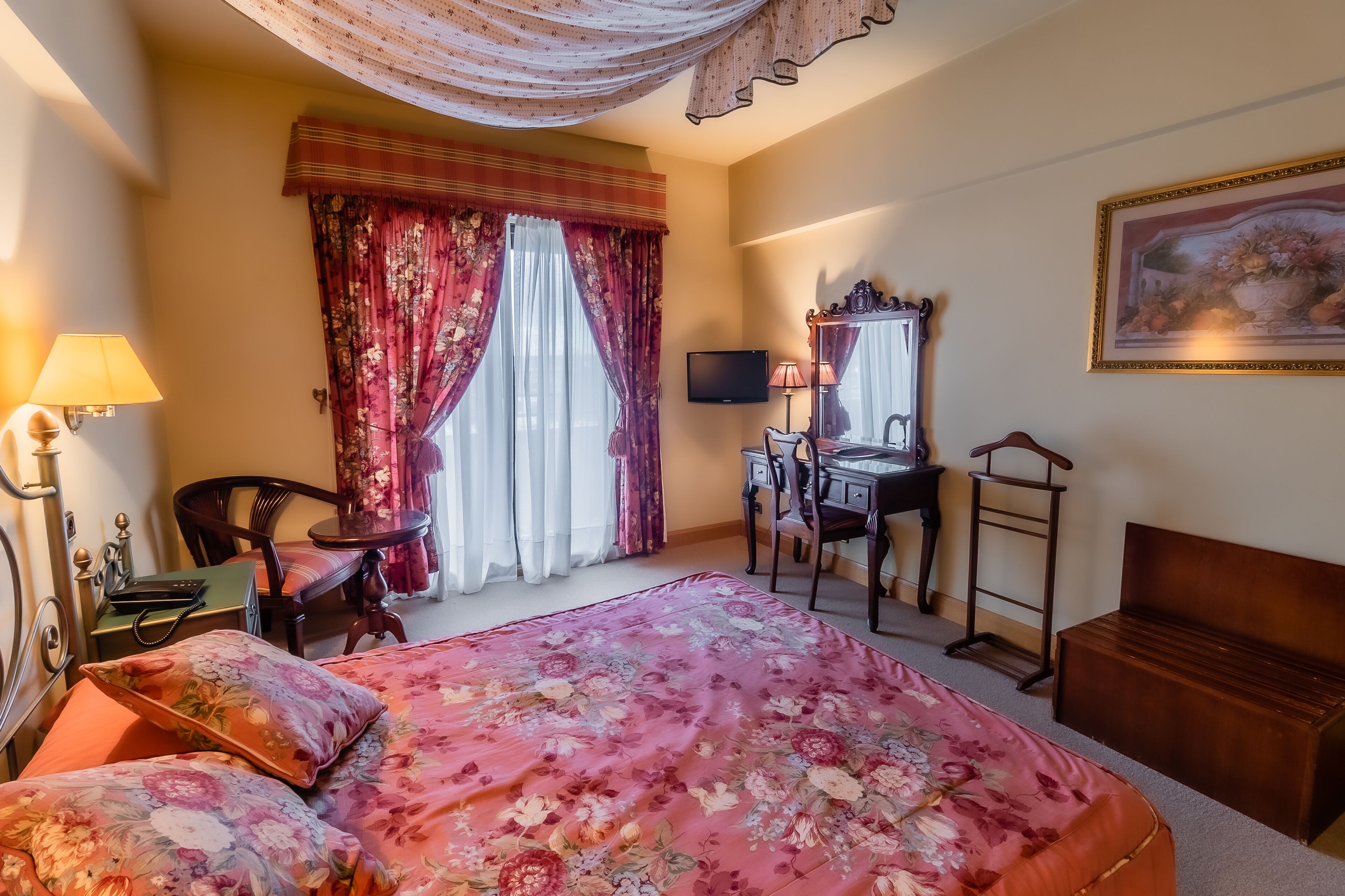 Een hotelkamer met een bed, een bureau, een stoel, een televisie en een schilderij aan de muur.