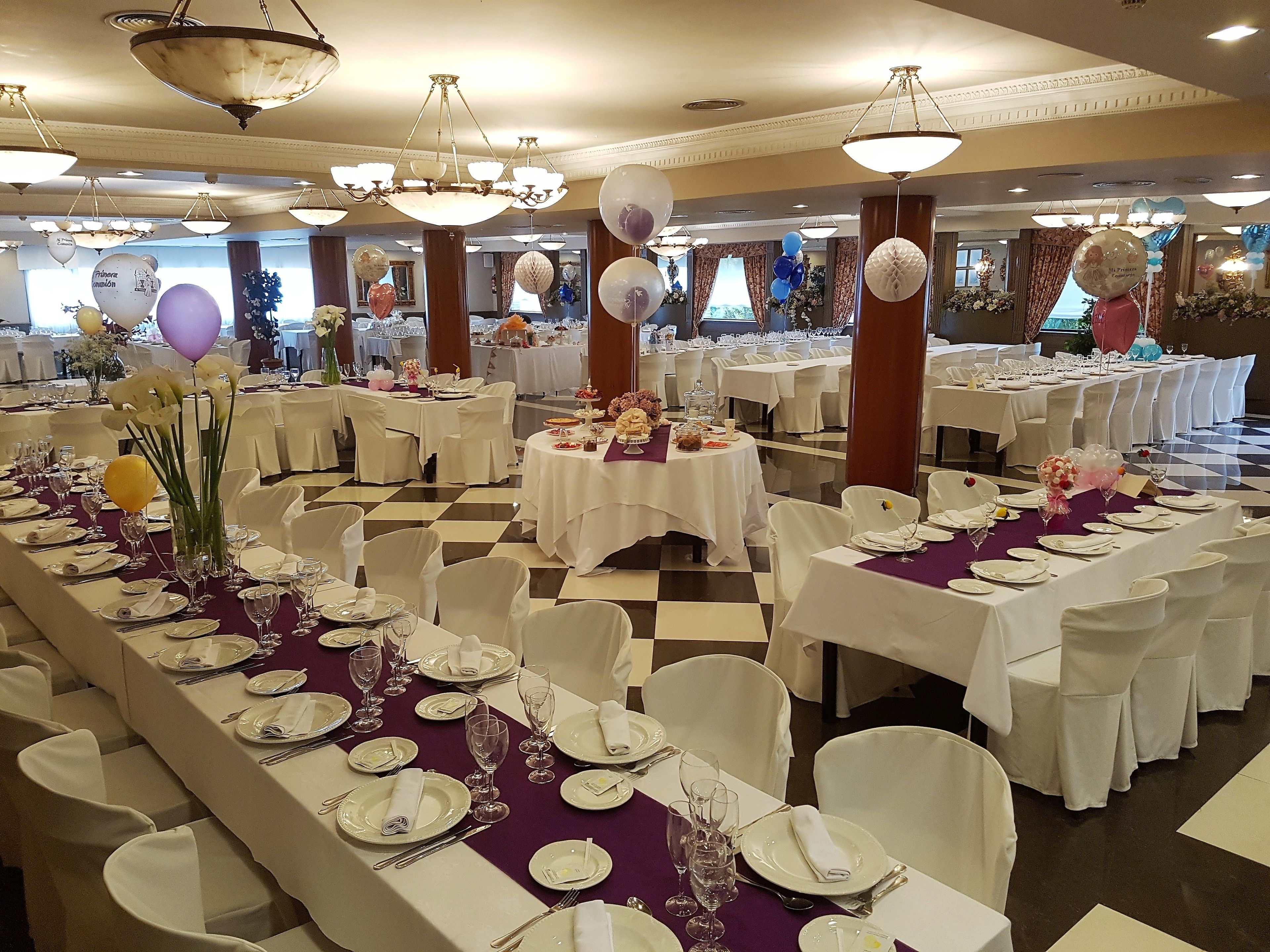 Un salón de banquetes con varias mesas redondas dispuestas para comer, manteles blancos y sillas blancas.