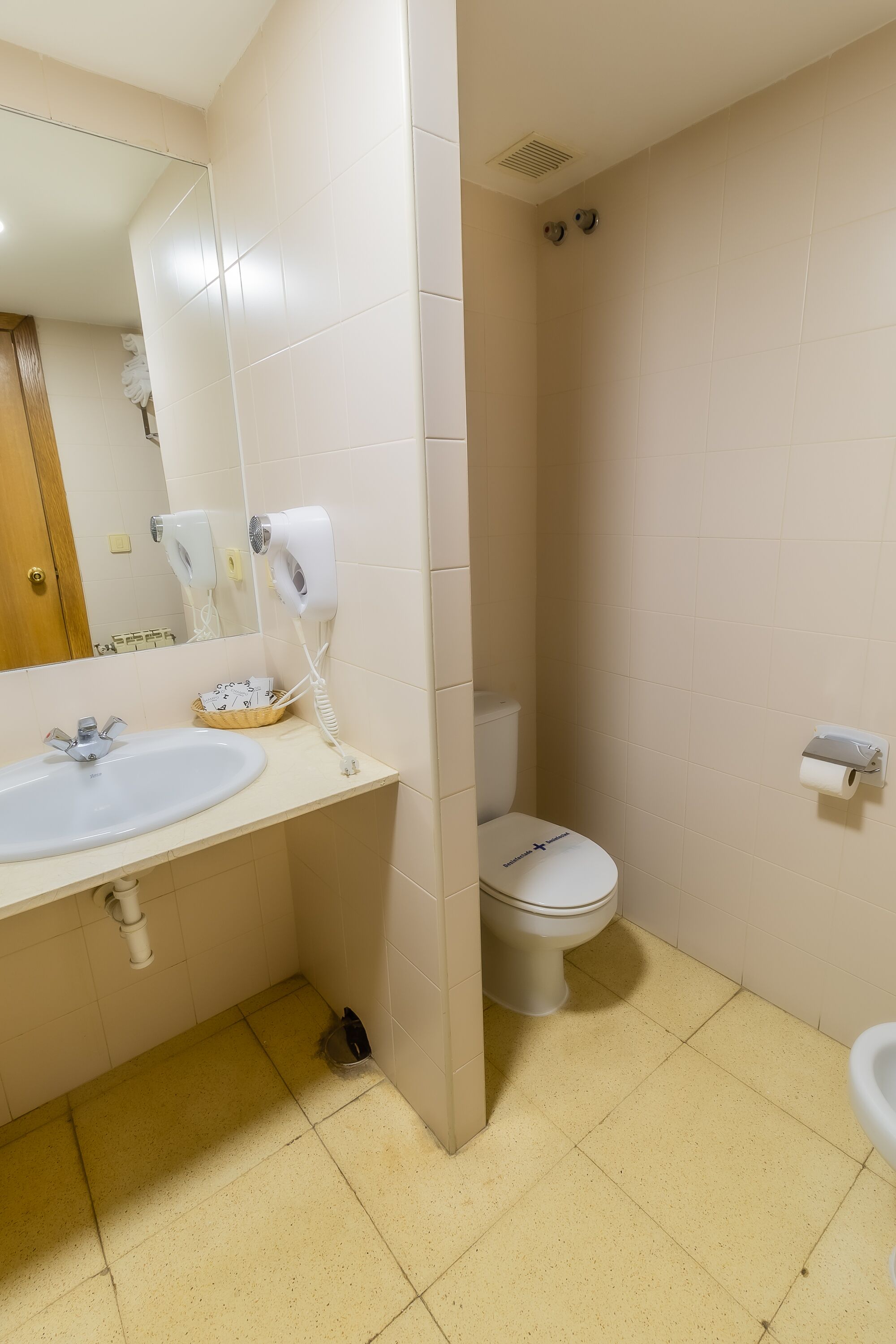 A bathroom with a sink, mirror, hair dryer, toilet, and a towel rack.
