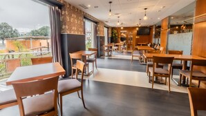 Un restaurante con mesas y sillas de madera, ventanas amplias y una decoración interior moderna.