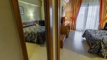 Una habitación de hotel con dos camas, un escritorio, una silla, una lámpara y una ventana con cortinas.