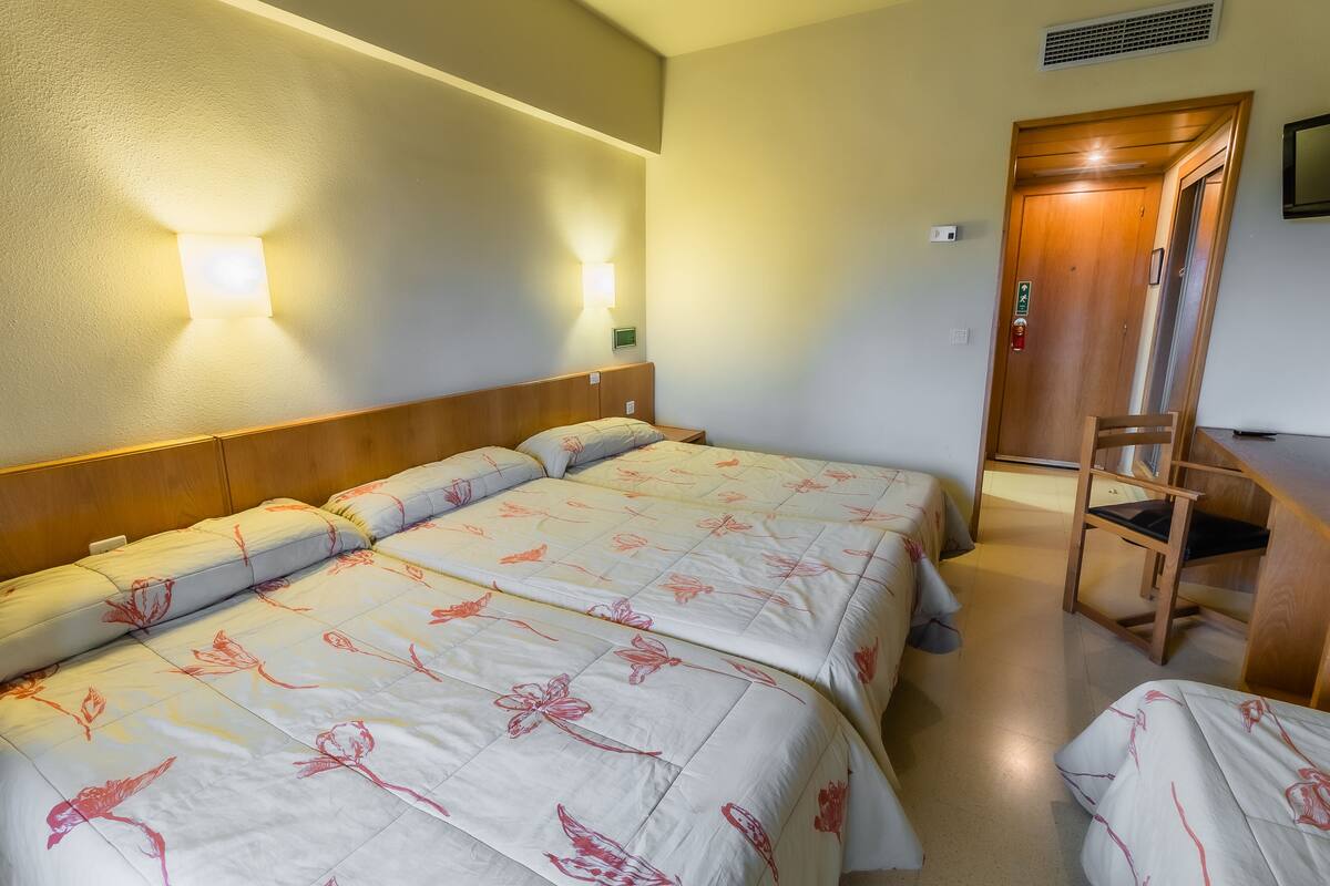 A hotel room with two beds, a wooden headboard, and a desk with a chair.