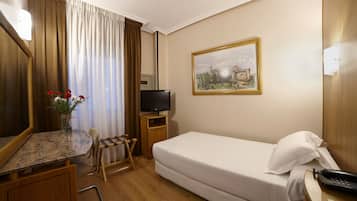 Habitación de hotel con cama, televisión, un cuadro, escritorio con silla y un jarrón de flores.