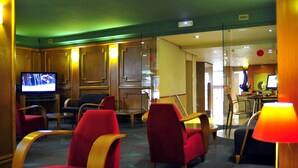 Un vestíbulo de hotel con sillas rojas y negras, un televisor y una zona de comedor con mesa y sillas.