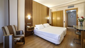 Habitación de hotel con cama doble, una silla, una mesita y un armario de madera.