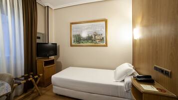 A hotel room with a bed, a television, a painting on the wall, and a desk with a telephone.