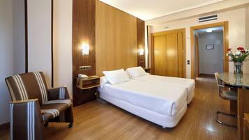A hotel room with a double bed, a chair, a small table, and a wooden wardrobe.