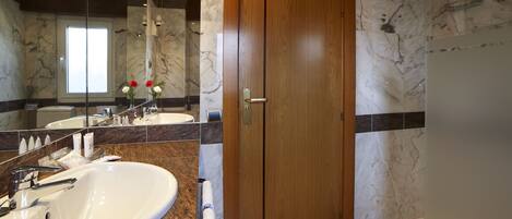 A bathroom with a marble floor, a wooden door, a large sink, and a mirror.