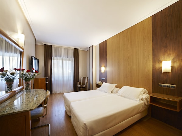 Una habitación de hotel con dos camas, un escritorio con silla, televisión y espejo.