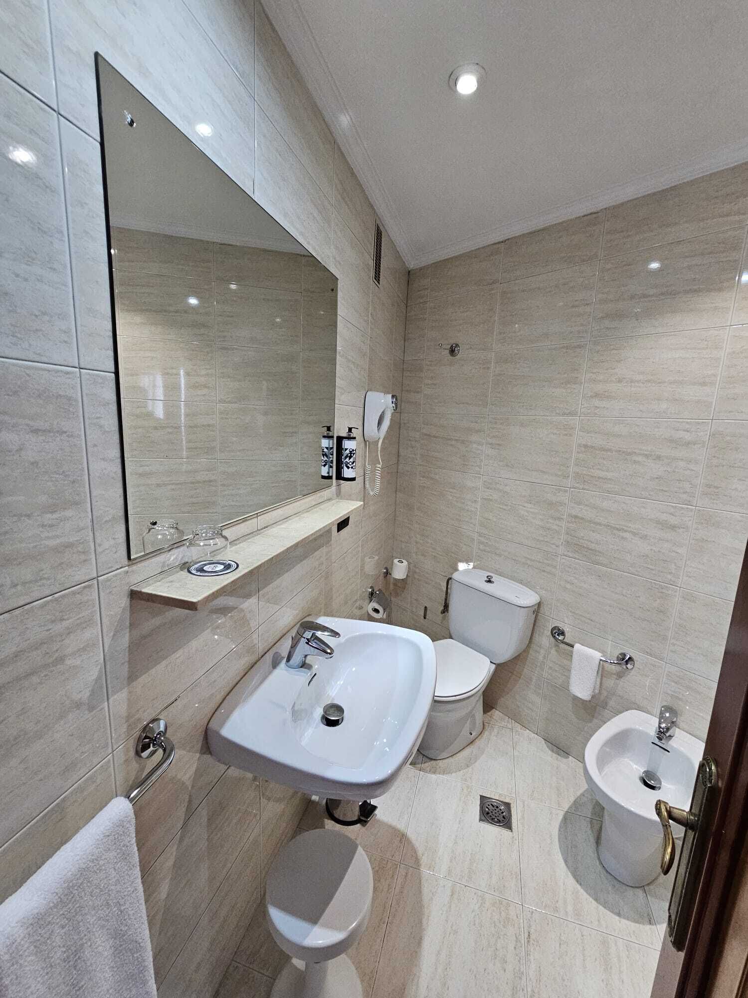 A modern bathroom with a large mirror, a sink, a toilet, and a bidet.
