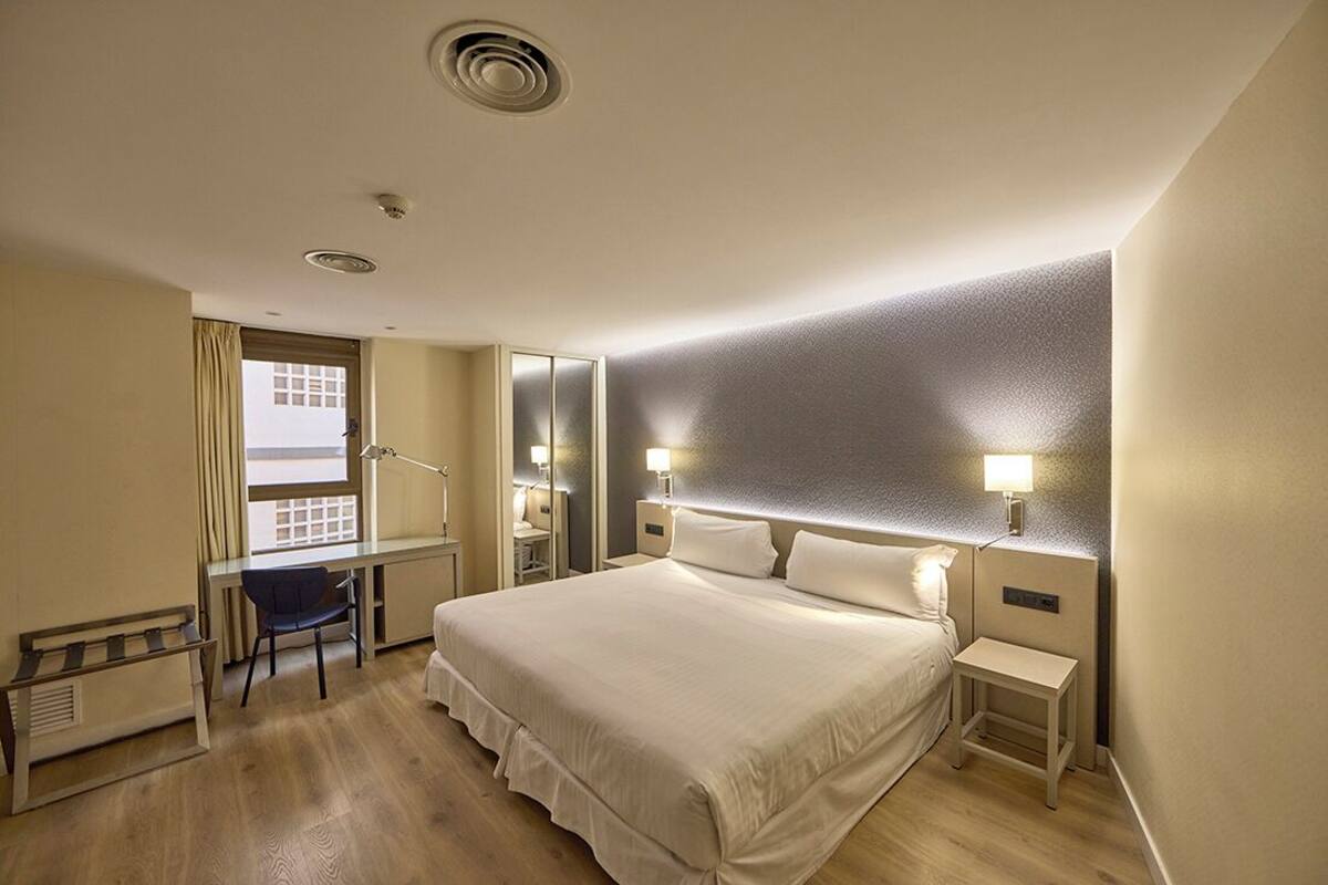 A hotel room with a large bed, a desk, a chair, and a window with curtains.