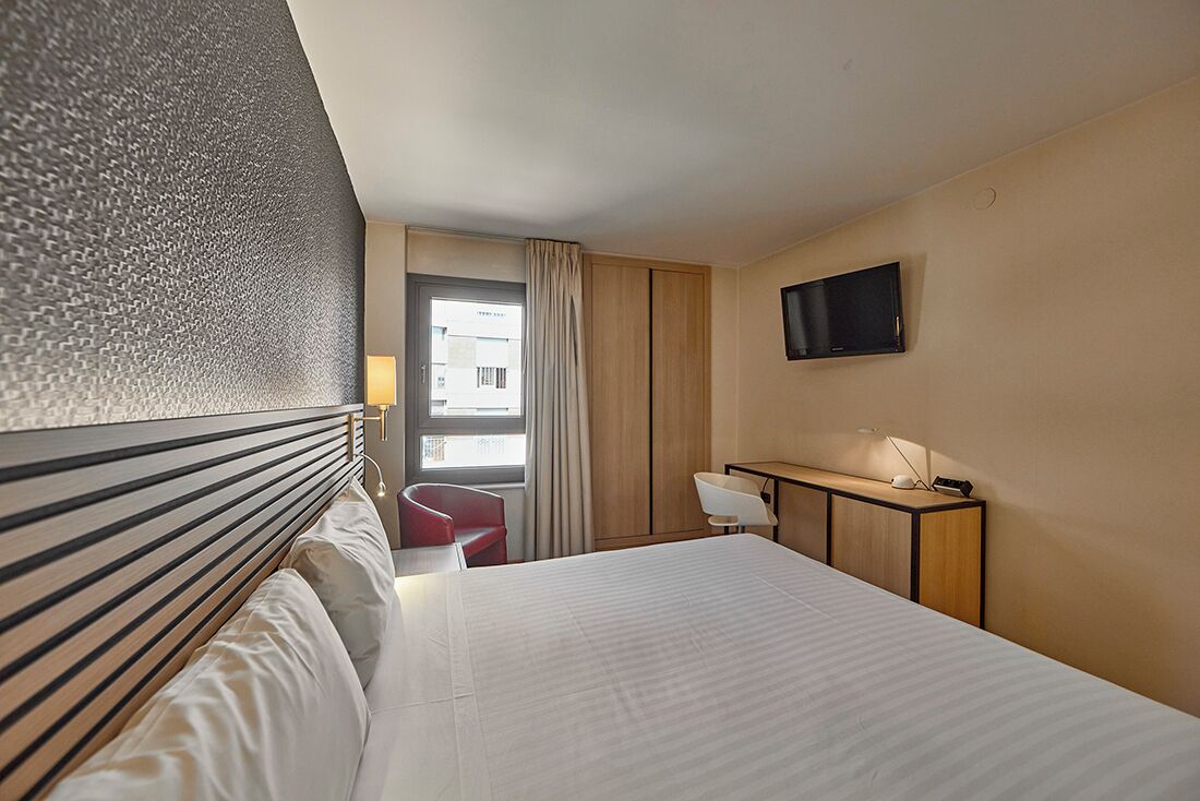 Een hotelkamer met een bed, bureau, stoel, televisie en raam met gordijnen.