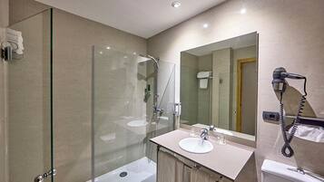 Un bagno moderno con doccia vetrata, lavabo con specchio e asciugacapelli a parete.