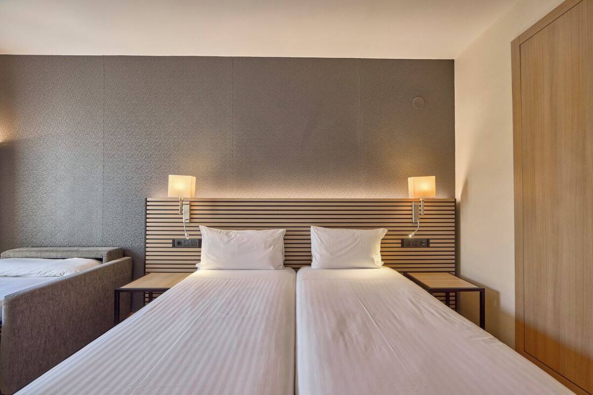 A hotel room with two beds, a small table, and a nightstand with a lamp.
