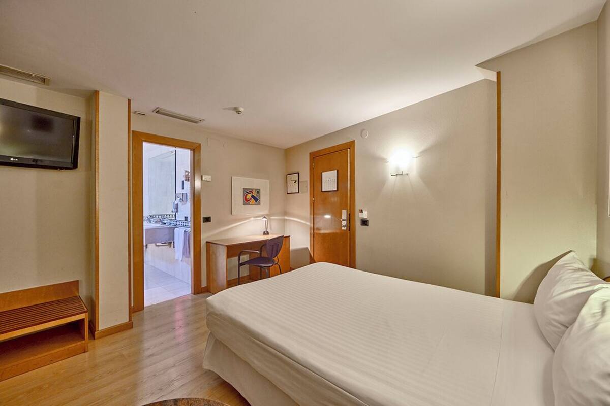 A hotel room with a bed, a desk, a chair, a television, and a door leading to a bathroom.