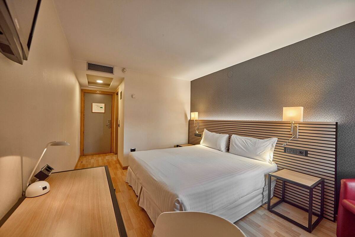 A hotel room with a large bed, bedside tables, a desk, and a chair.