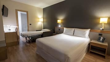 A hotel room with a large bed, two bedside tables with lamps, a desk with a chair, and a television on the wall.