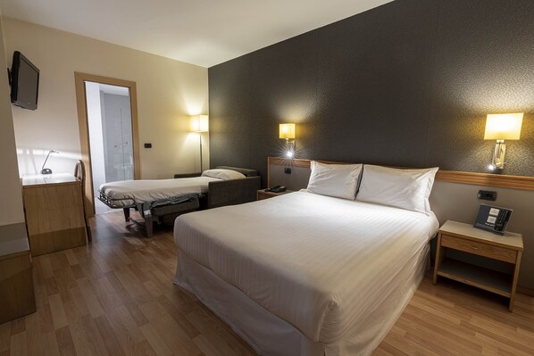 Habitación de hotel con una cama grande, dos mesitas de noche con lámparas, un escritorio con silla y un televisor en la pared.