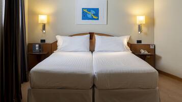 Cama doble con ropa de cama blanca, dos mesitas de noche con lámparas, una obra enmarcada sobre la cama y suelo de madera.