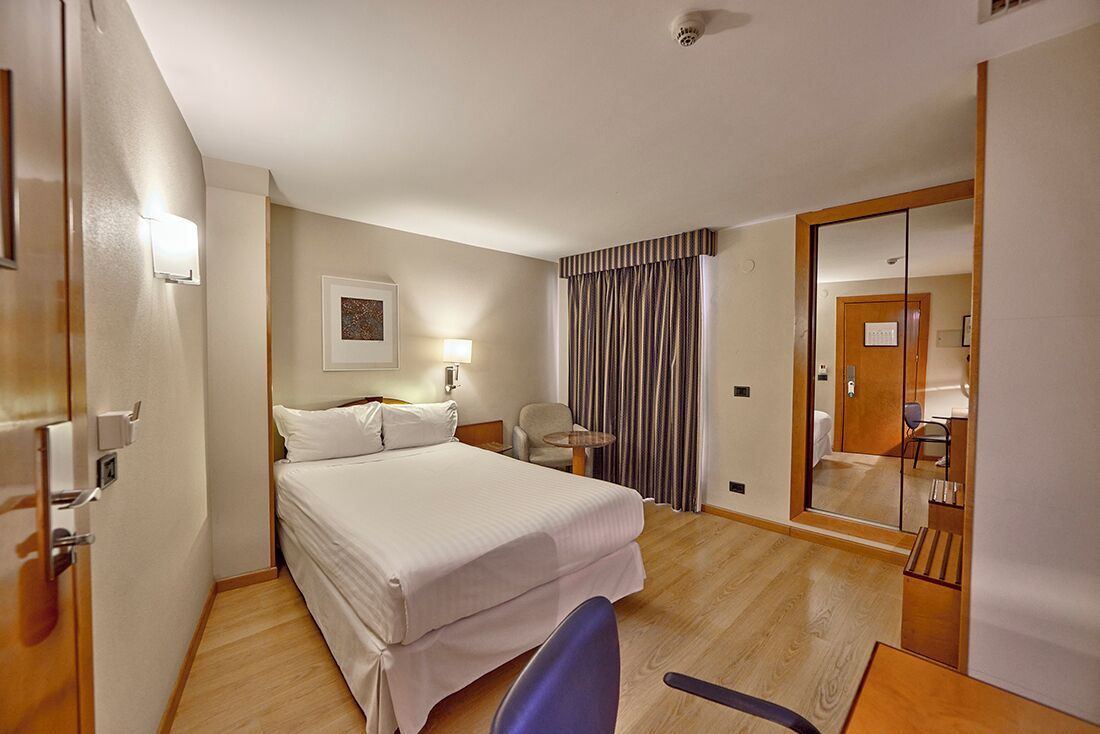 Una habitación de hotel con cama, escritorio, silla, espejo y puerta.