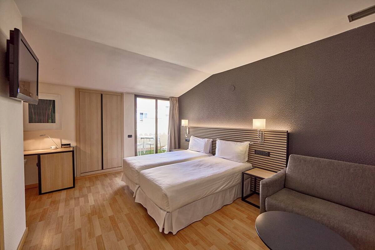 A hotel room with two beds, a desk, a TV, and a sofa.