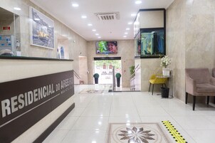 A hotel reception area with a reception desk, a TV screen, and a seating area with a chair and a small table.