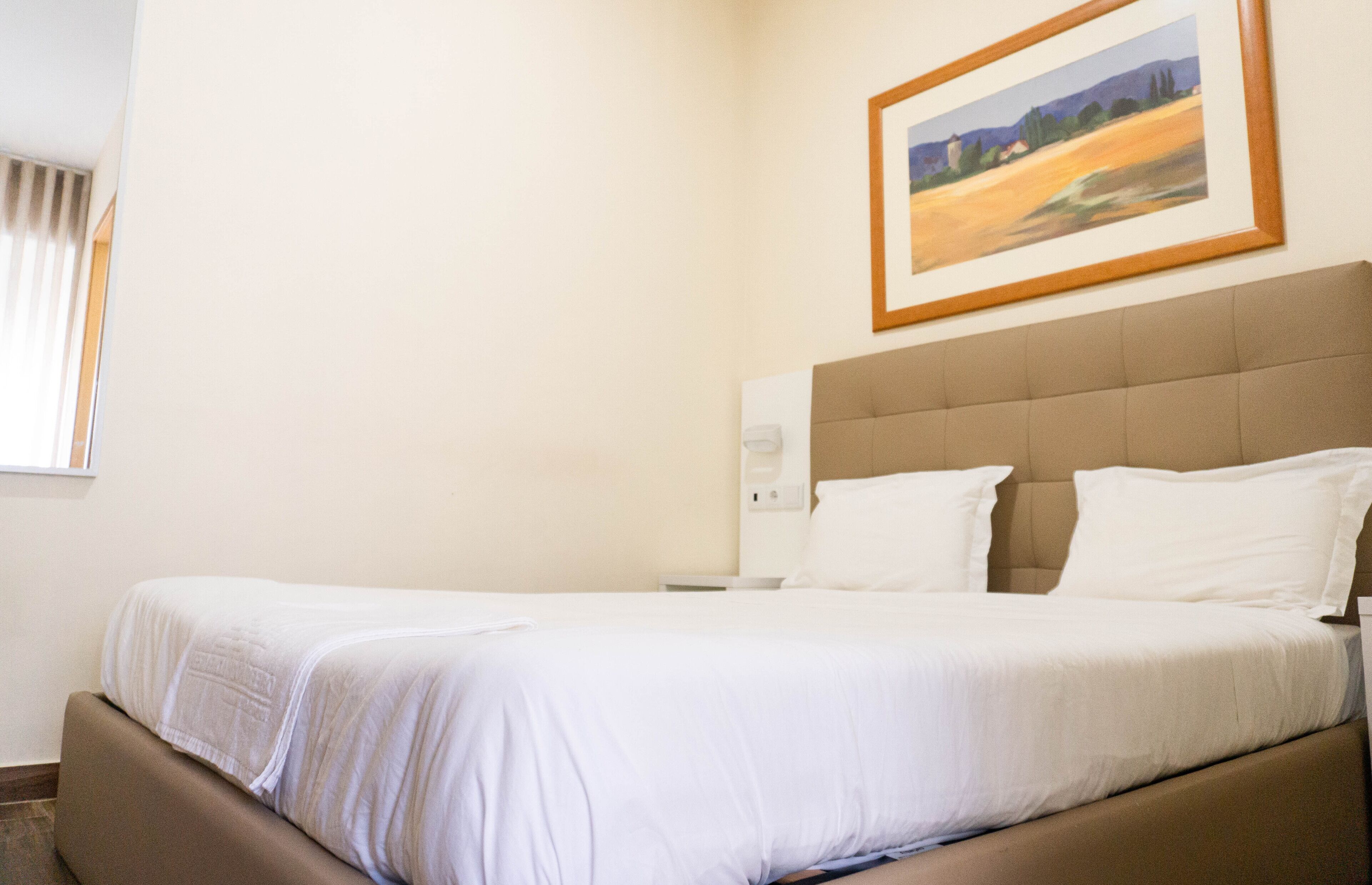 A hotel room with a large bed, a headboard, and a framed painting on the wall.