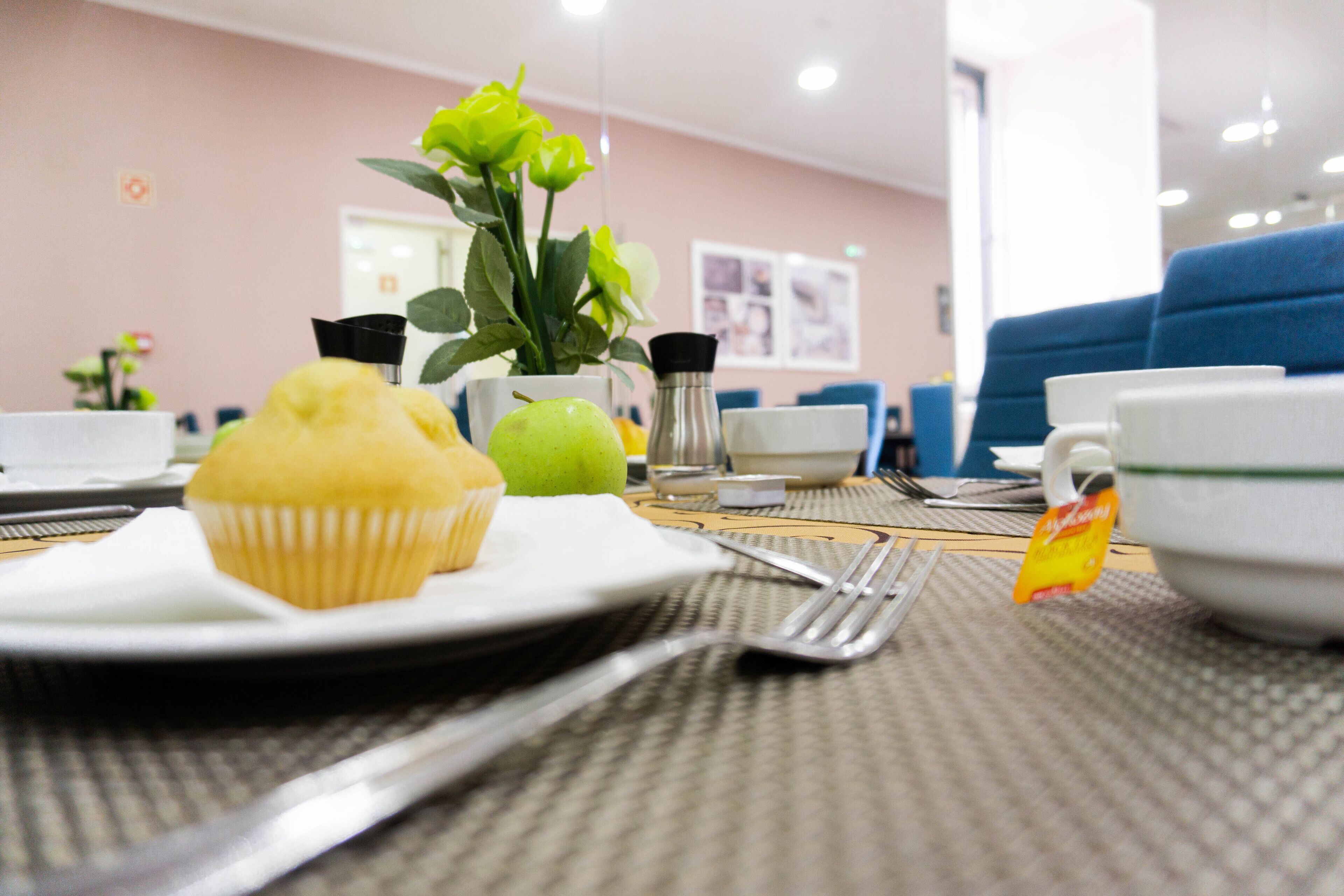 Un desayuno con un muffin, una manzana verde y una bolsita de té sobre una mesa.