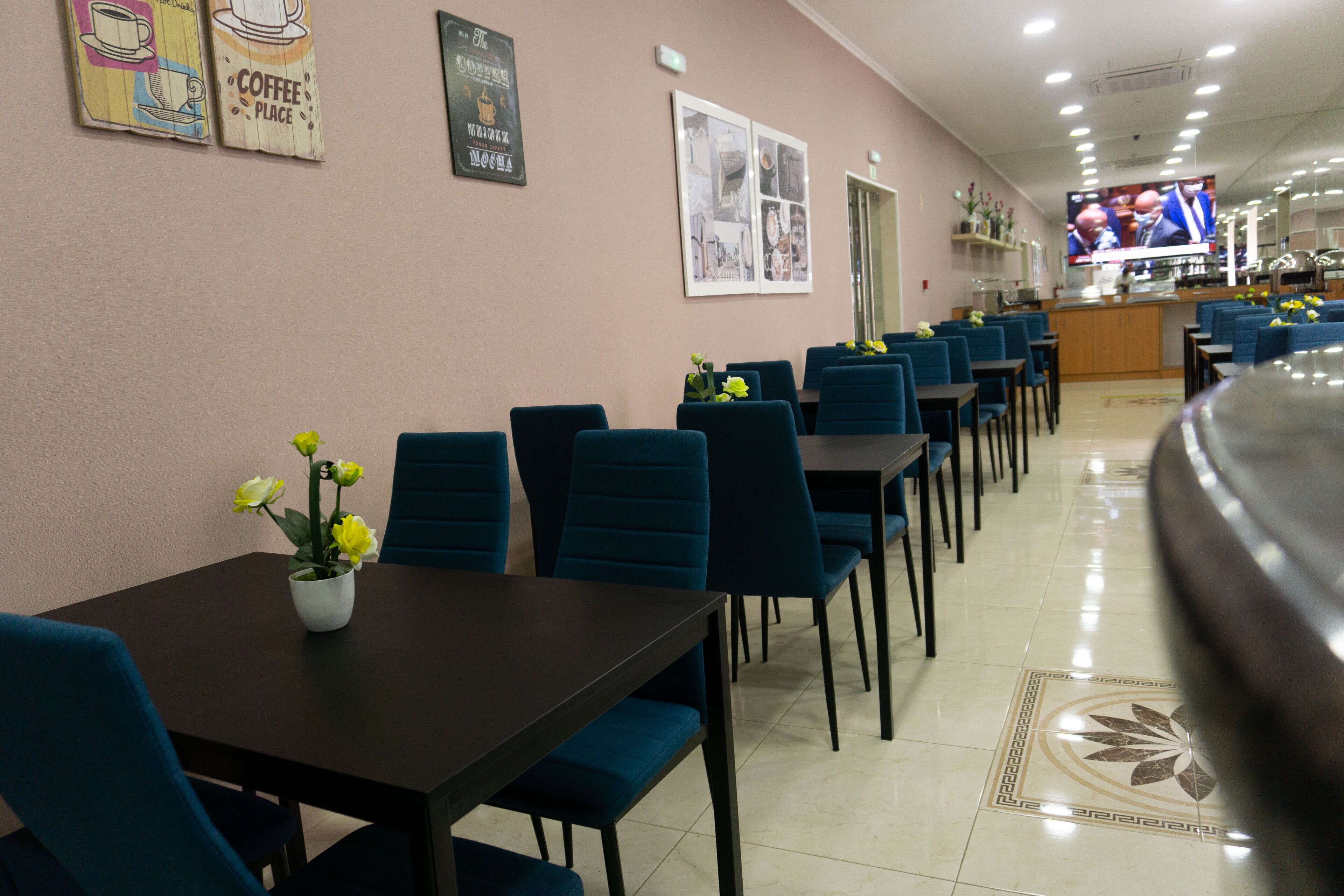 A restaurant with blue chairs, a coffee-themed wall, and a TV screen.