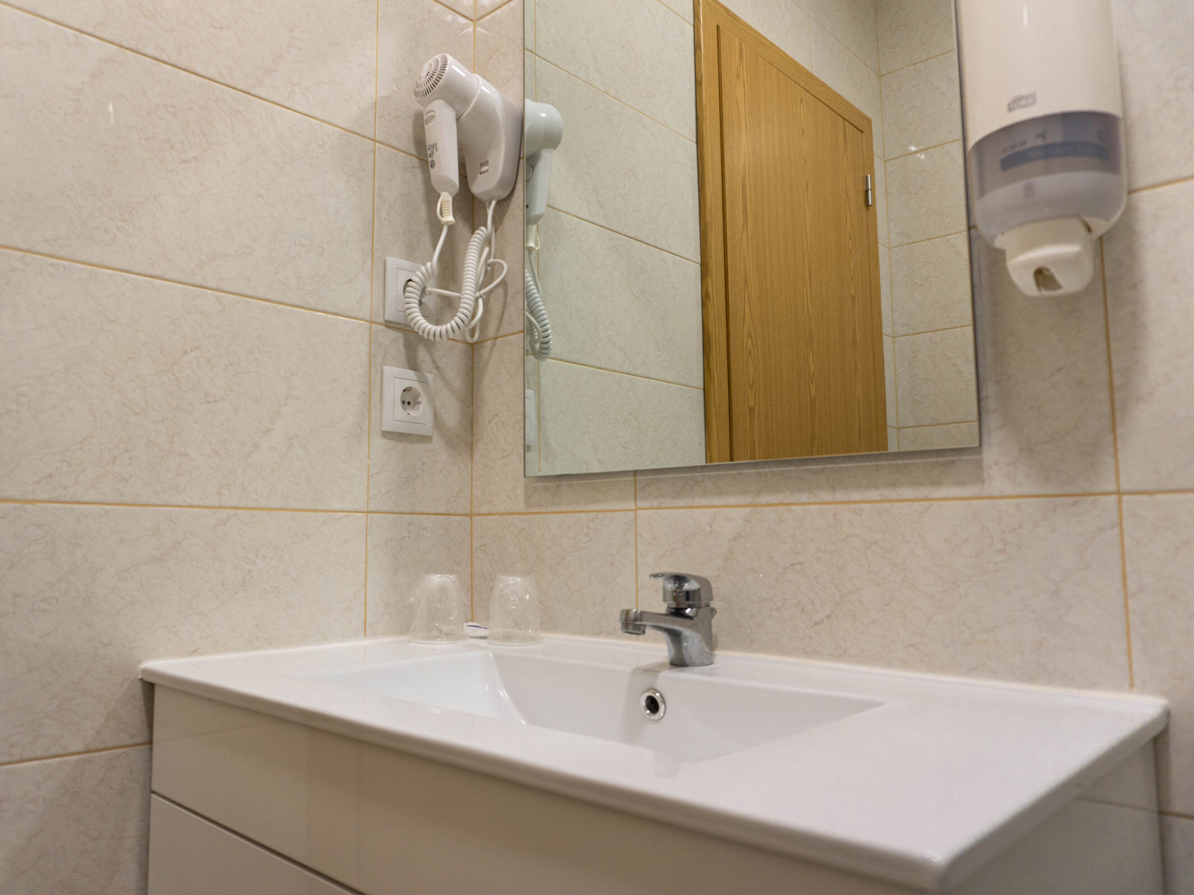 Een badkamer met een wit wastafel, een spiegel, een haardroger en een handdroger.
