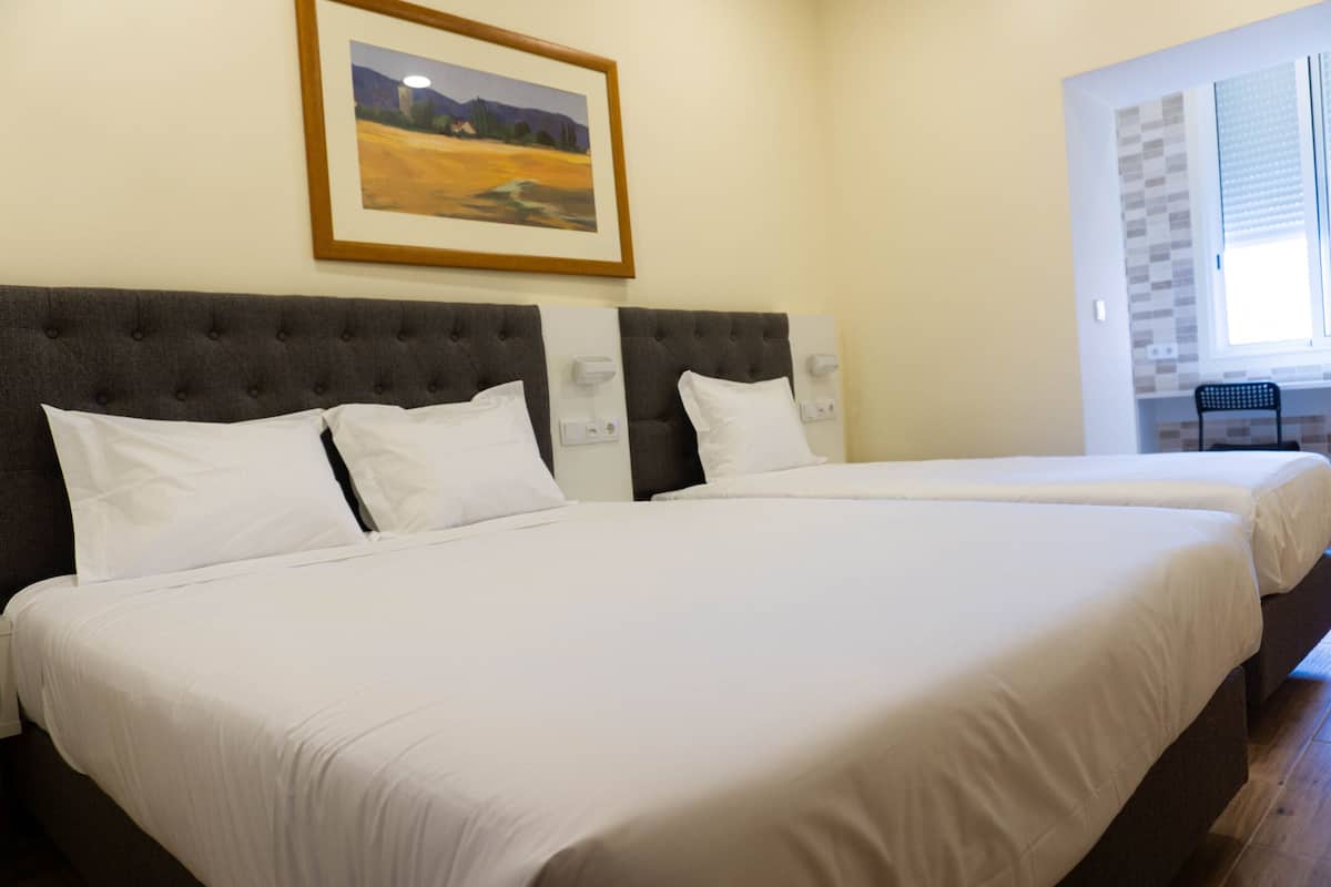 A hotel room with two beds, a framed painting on the wall, and a window with blinds.