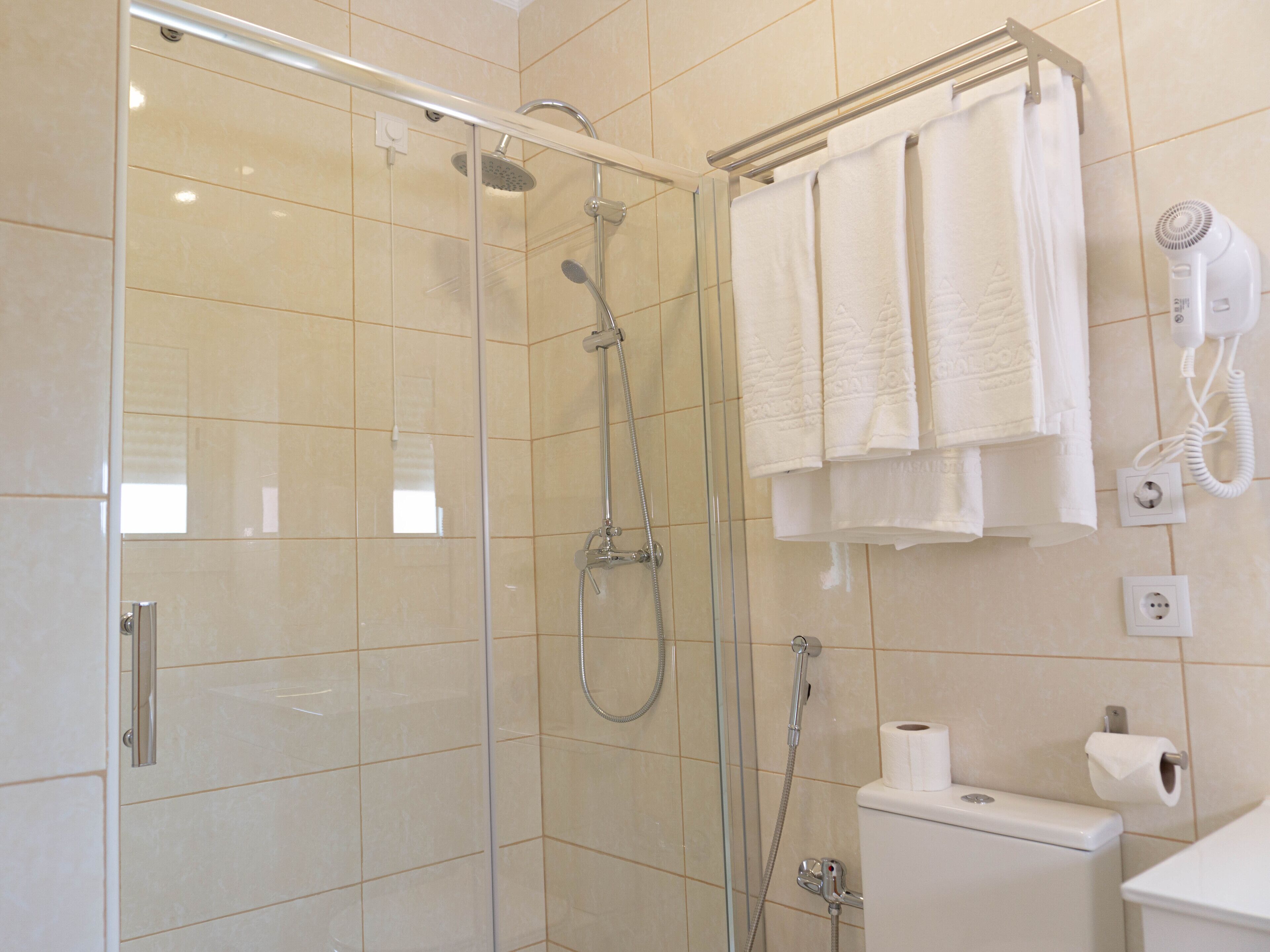 Un baño moderno con ducha envuelta en vidrio, inodoro y toallero con varias toallas.