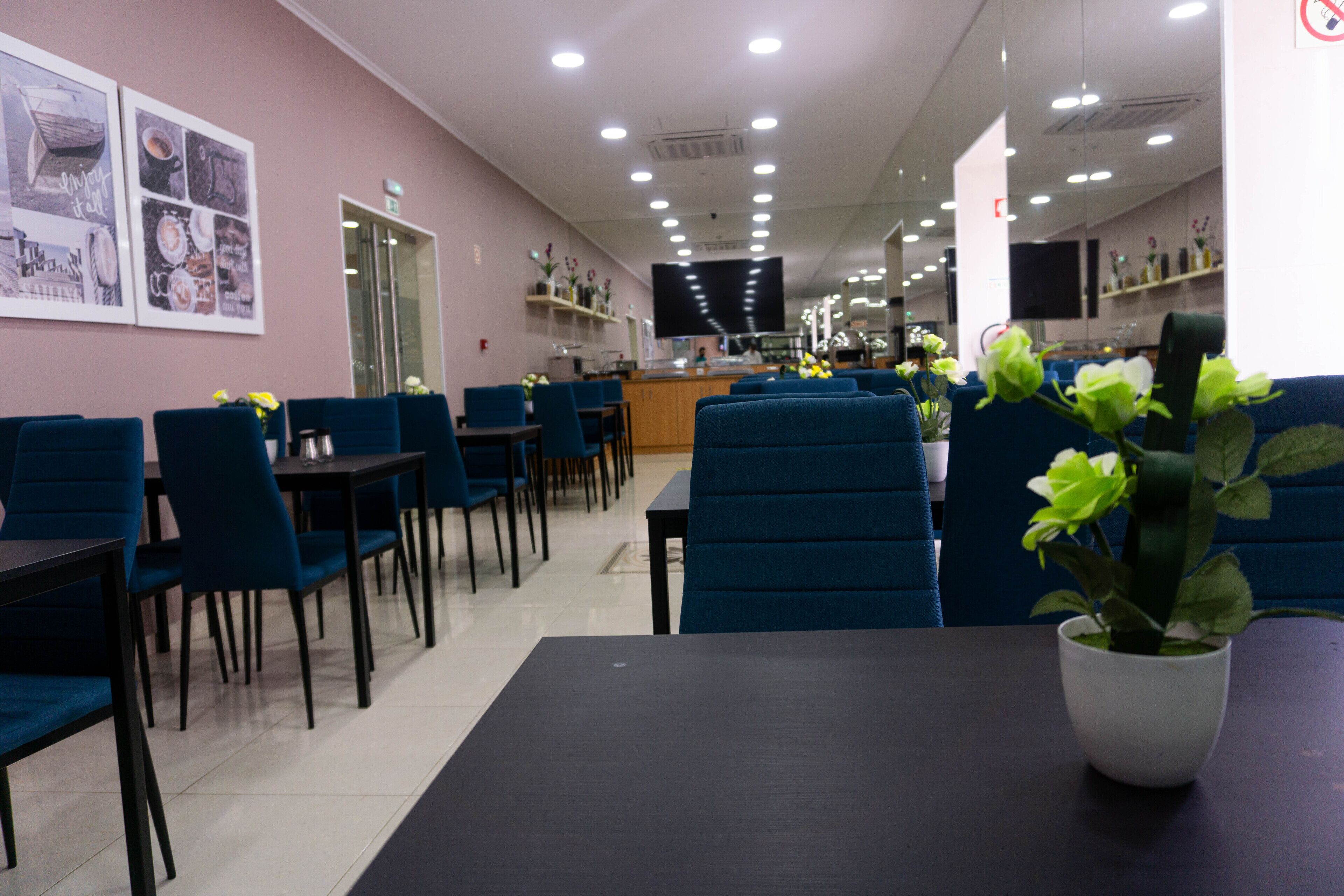 A restaurant with blue chairs and tables, a counter, and a TV screen.