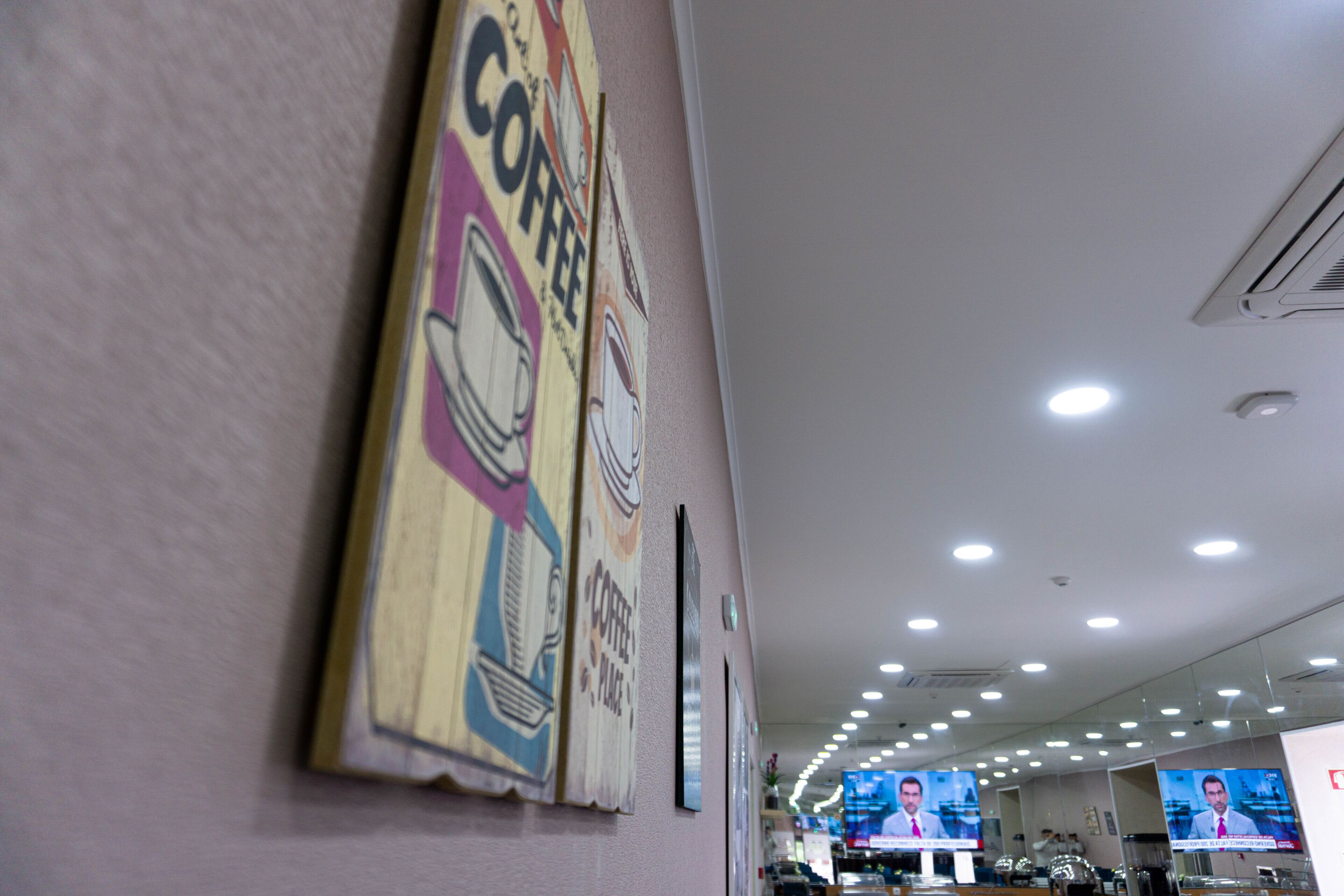 Un couloir agrémenté d’une décoration murale sur le thème du café, d’un écran de télévision diffusant un journal télévisé et d’un plafond doté d’un éclairage encastré.