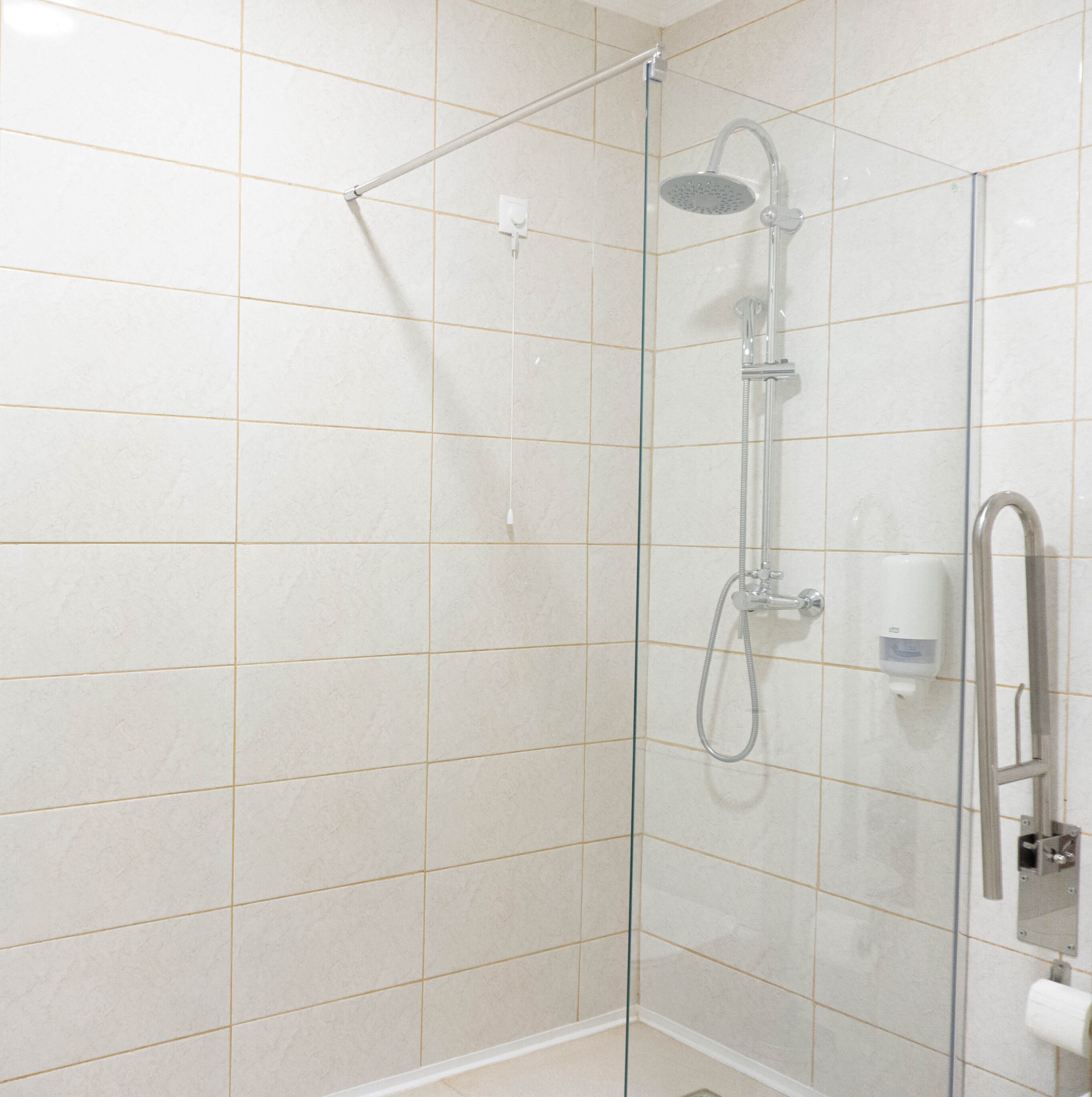 Un espace douche fermé par des parois en verre, équipé d’un pommeau de douche à main, d’un flexible de douche et d’un distributeur de savon fixé au mur.