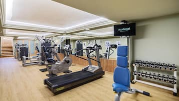 Un gimnasio con máquinas de cardio, bancos de pesas y mancuernas.