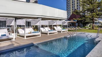 A poolside area with lounge chairs and umbrellas, a clear pool, and a building in the background.