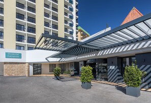 A modern hotel entrance with a covered walkway, a sign for 'Occidental Fuengirola', and a view of a high-rise building with a red-tiled roof. - Occidental Fuengirola (Fuengirola)
