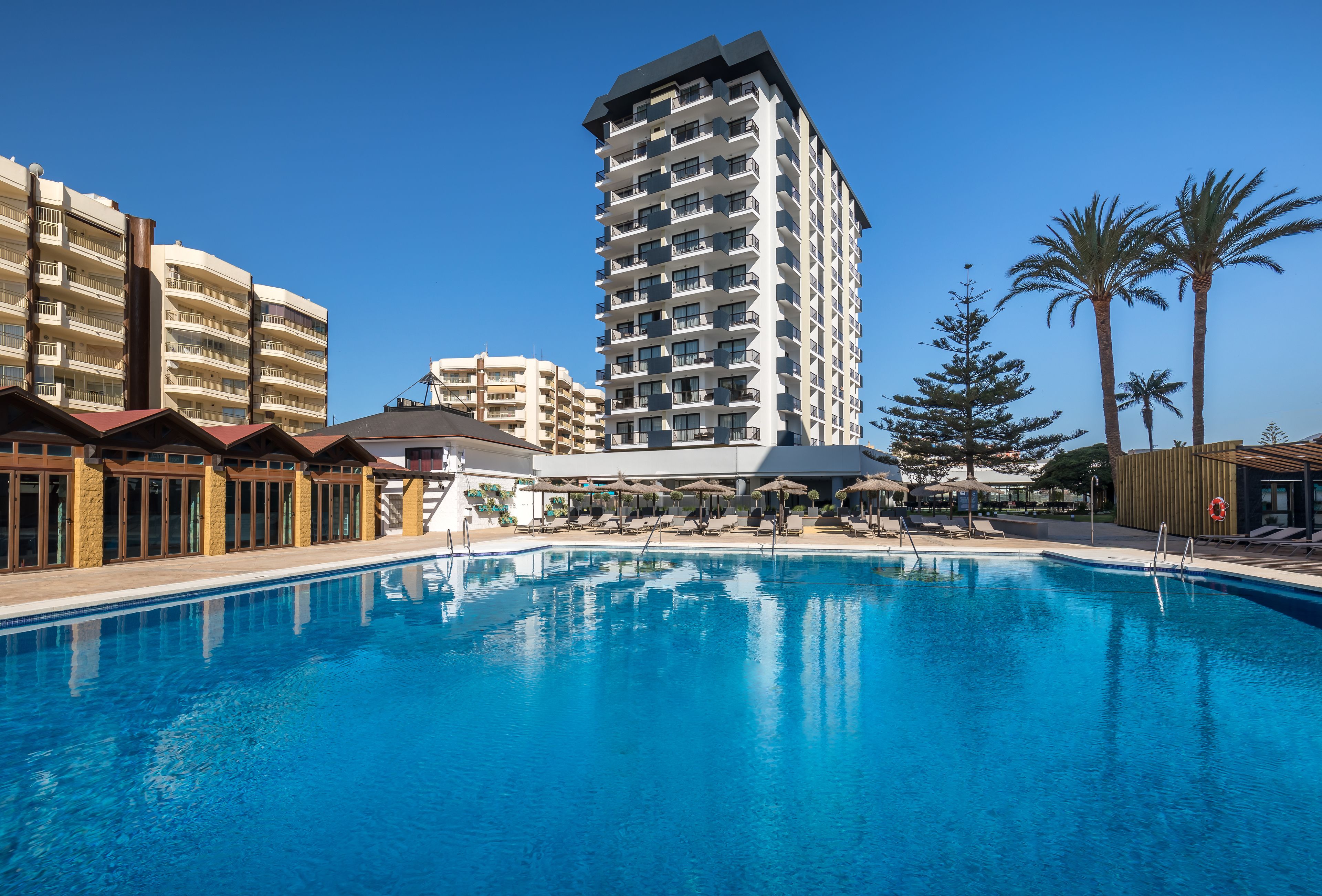 Een hotel met een zwembad, meerdere balkons en palmbomen.