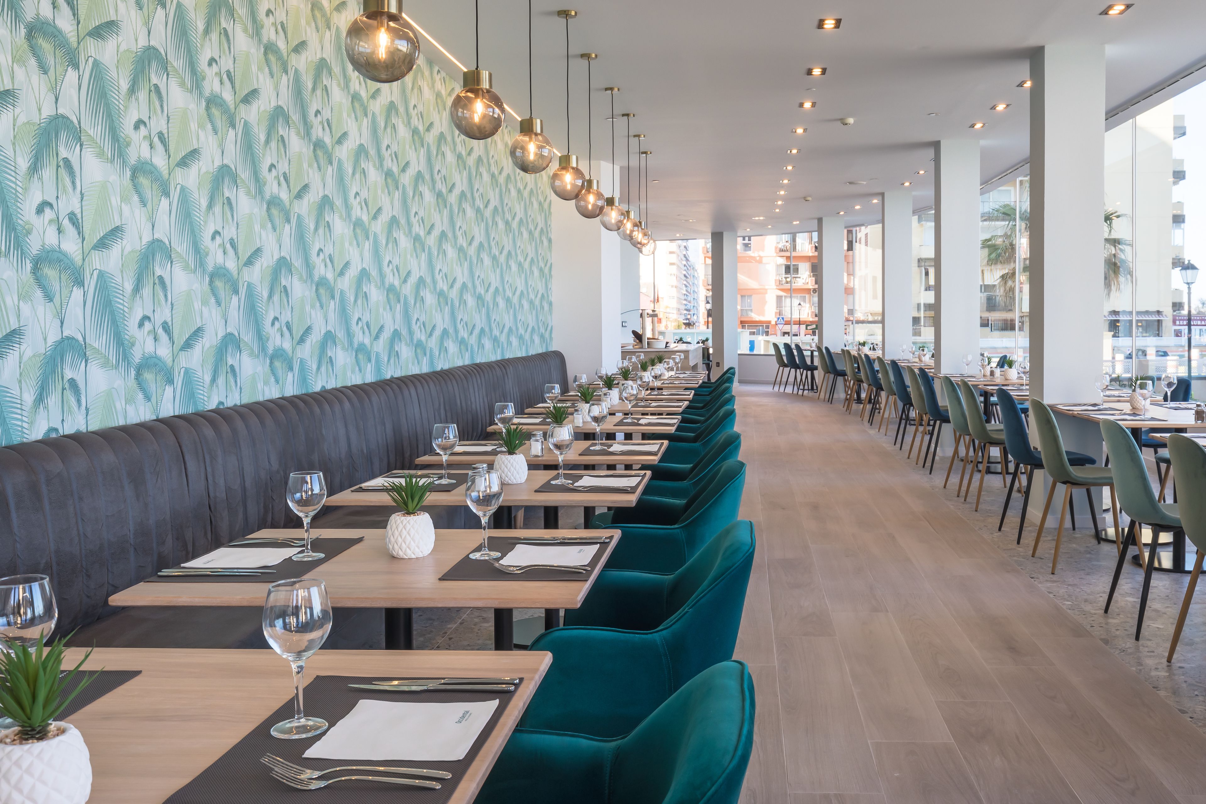 Un restaurante con mesas largas, sillas color turquesa y una pared con diseño.