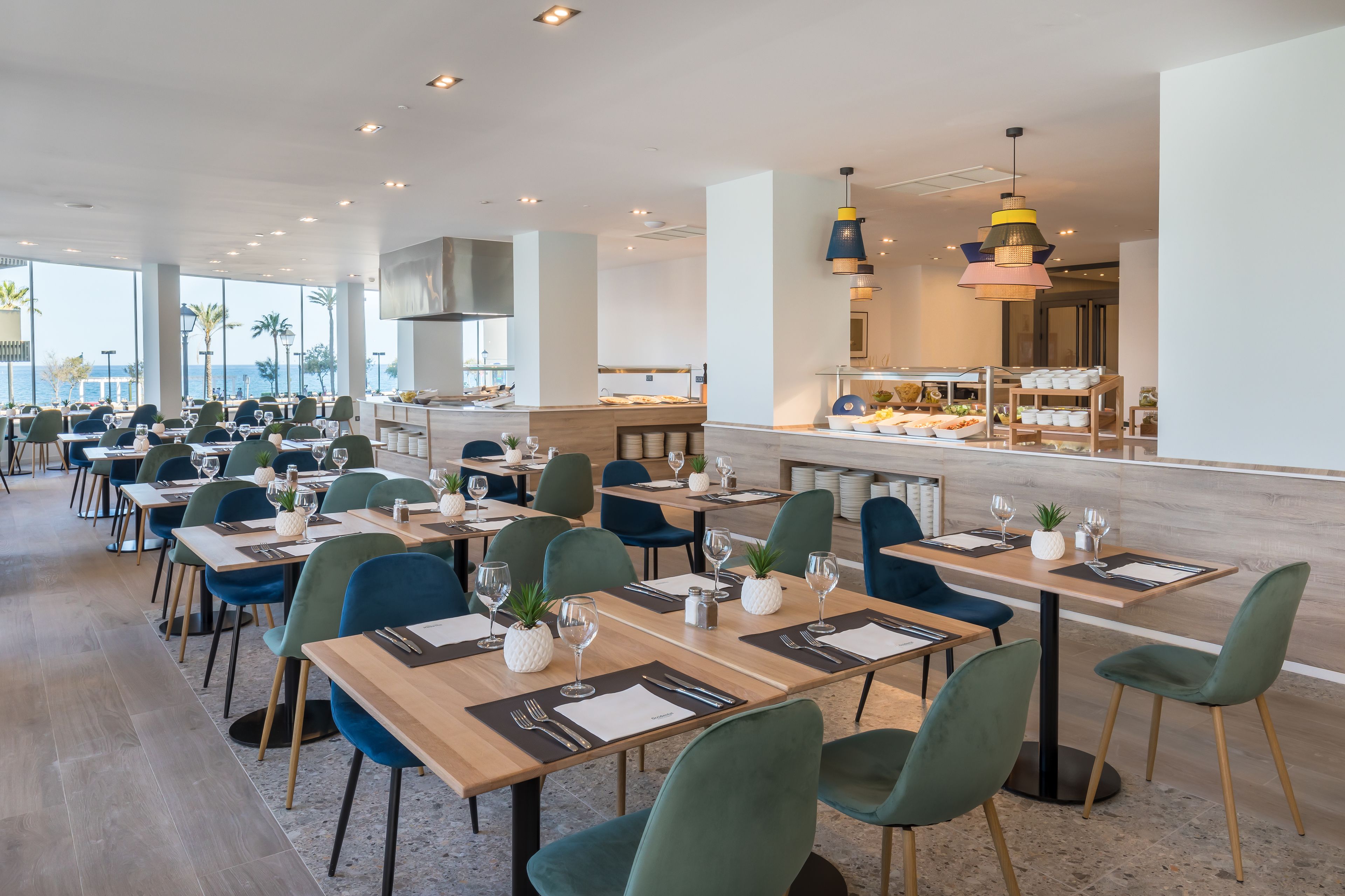 Un restaurante moderno con varias mesas, sillas verdes y vista al océano.