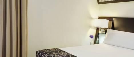 A hotel room with a bed, a nightstand, a lamp, and a wall-mounted picture.