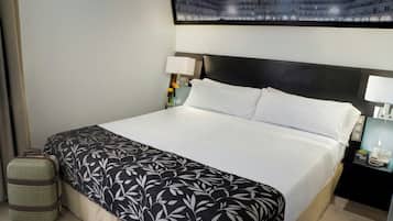 Una habitación de hotel con cama, mesita de noche, lámpara, maleta y una obra de arte colgada en la pared.