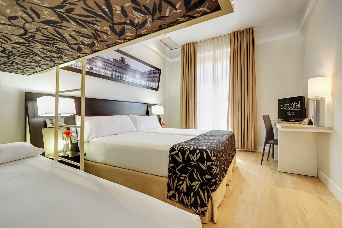 A hotel room with a bed, a desk, a chair, a television, and a decorative ceiling.