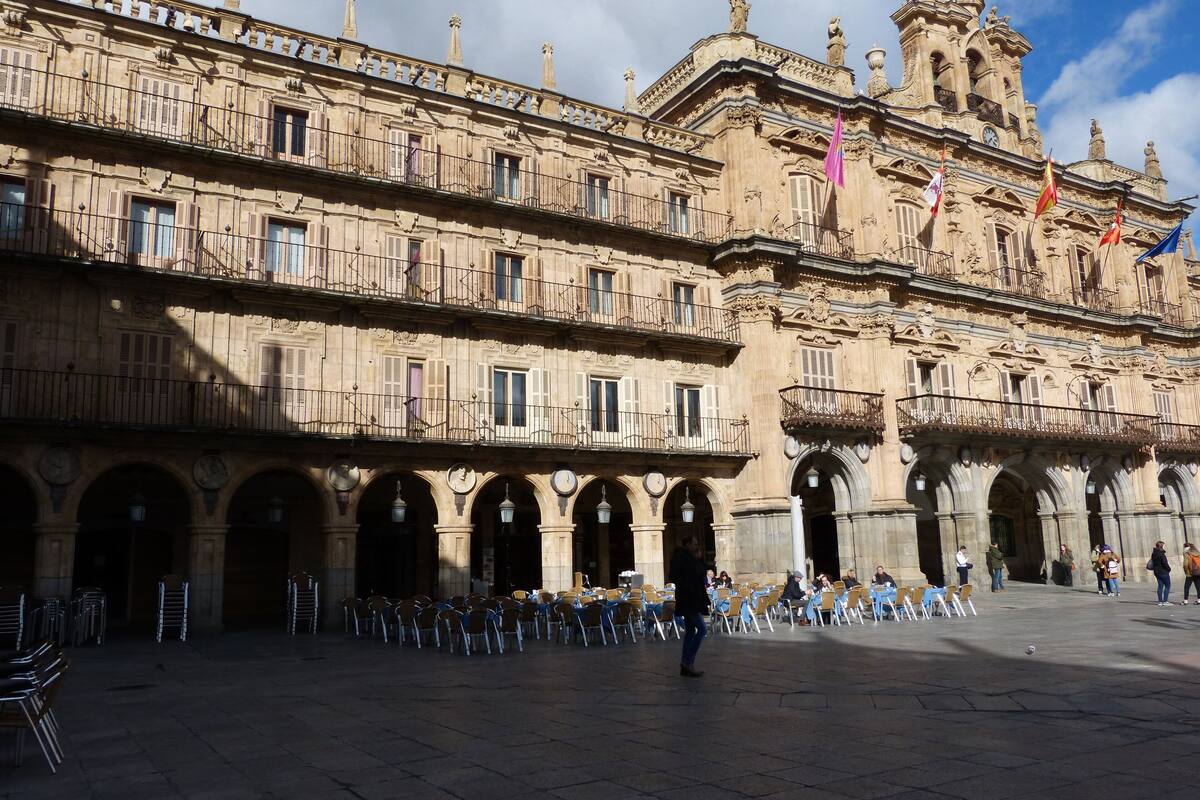 A historic building with multiple balconies and arches, a courtyard with outdoor seating, and flags.