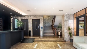 A modern lobby with a marble floor, a reception desk, a staircase, and a seating area. - Hotel Leuka (Alicante)