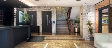 Eine moderne Lobby mit Marmorboden, einer Rezeption, einer Treppe und einer Sitzecke.